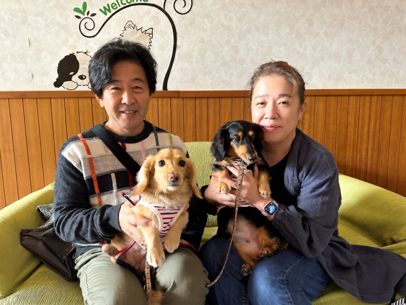 愛犬である2匹の保護犬（ミニチュアダックスフンドのメープルとオレ）と笑顔で触れ合う高倉秀和。